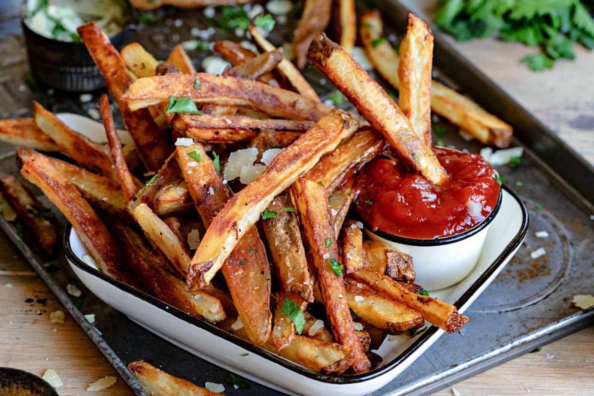 crispy oven fries sitting on white plate with small container of ketchup.