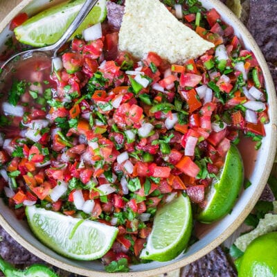 top down view of pico de gallo in clay bowl garnished with lime wedges and surrounded by chips.