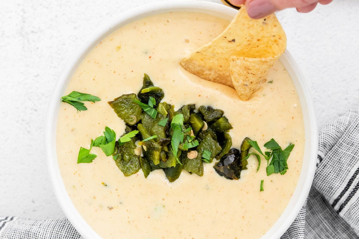 top down look at queso blanco in a white bowl topped with cilantro and peppers with a chip being dipped into the queso.