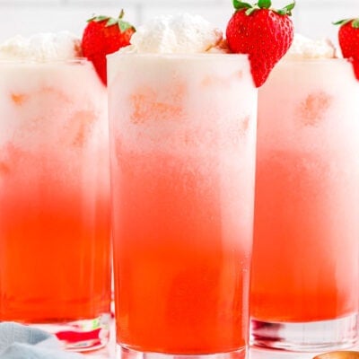 strawberry italian sodas in tall glasses garnished with whipped cream and fresh strawberries.