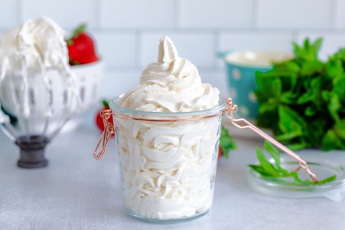 whipped cream piped into a small glass jar with a lid. mint and strawberries in background.