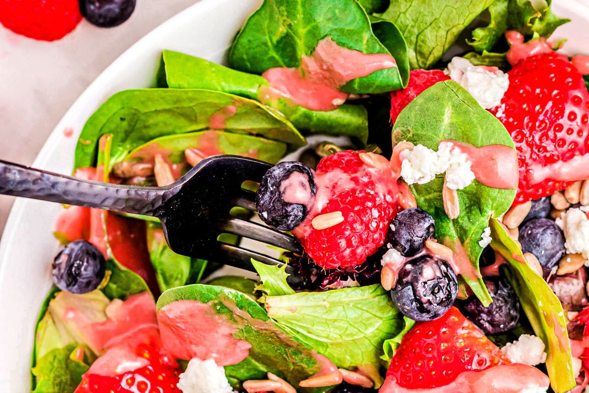 forkful of berry salad with spinach and goat cheese in bowl.