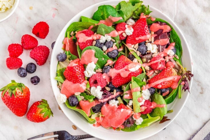 top down look at berry salad with raspberry vinaigrette dressing on white plate.