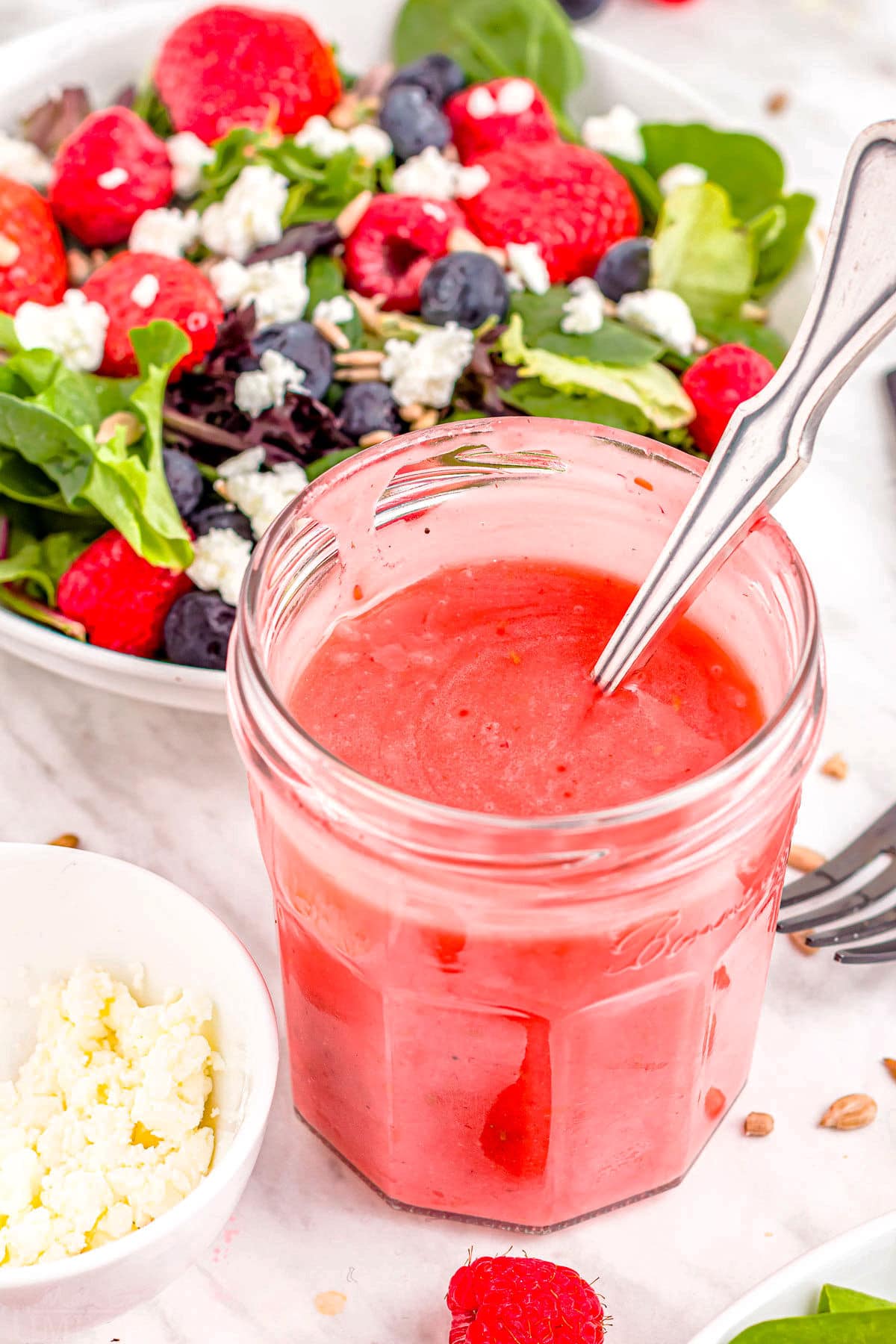 jar of raspberry dressing in front of a bowl of salad.