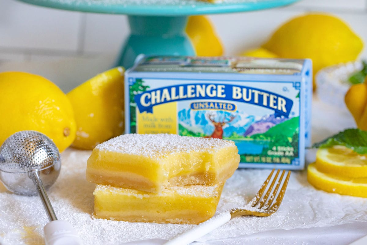 two lemon bars one with a bite taken out of it. box of challenge butter behind bars.