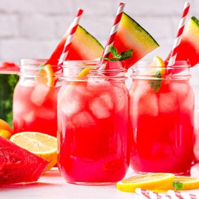 three large canning jars filled with watermelon lemonade and topped with watermelon wedges.