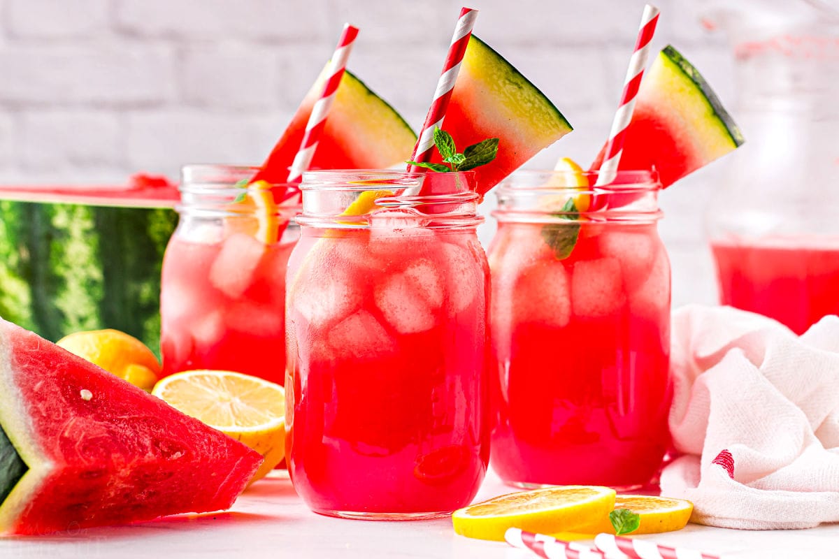 three large canning jars filled with watermelon lemonade and topped with watermelon wedges. 
