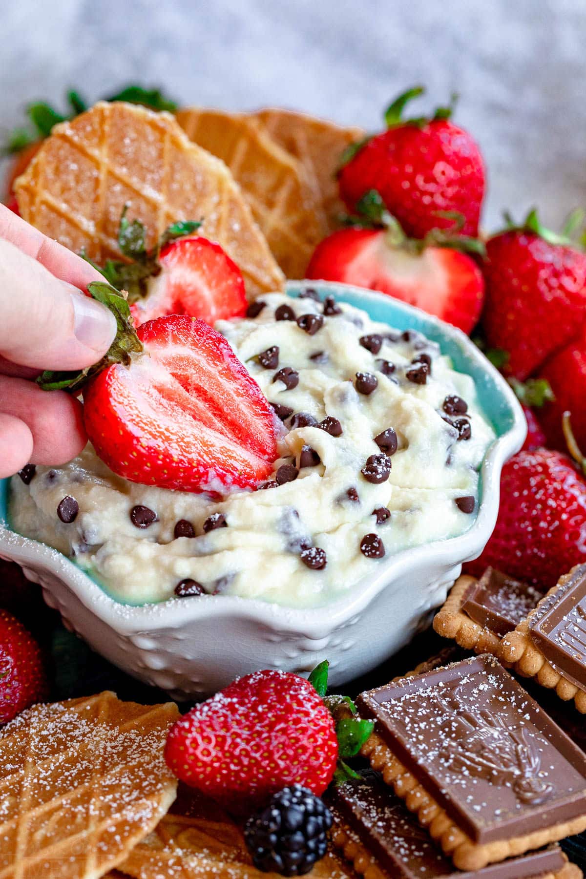 strawberry half being dipped into a bowl of cannoli dip.