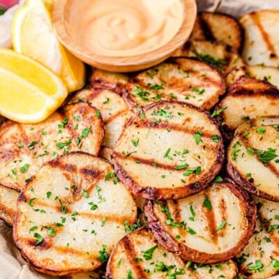 grilled potatoes served with spicy mayo dip and lemon wedges on wood tray.