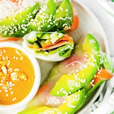 top down look at summer rolls on white plate with one cut in half. peanut dipping sauce in small bowl on the plate too.