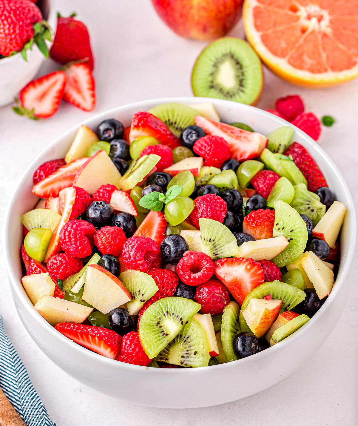 beautiful vibrantly colored fruit salad in white serving bowl. raspberries, kiwis, apples, blueberries and strawberries.