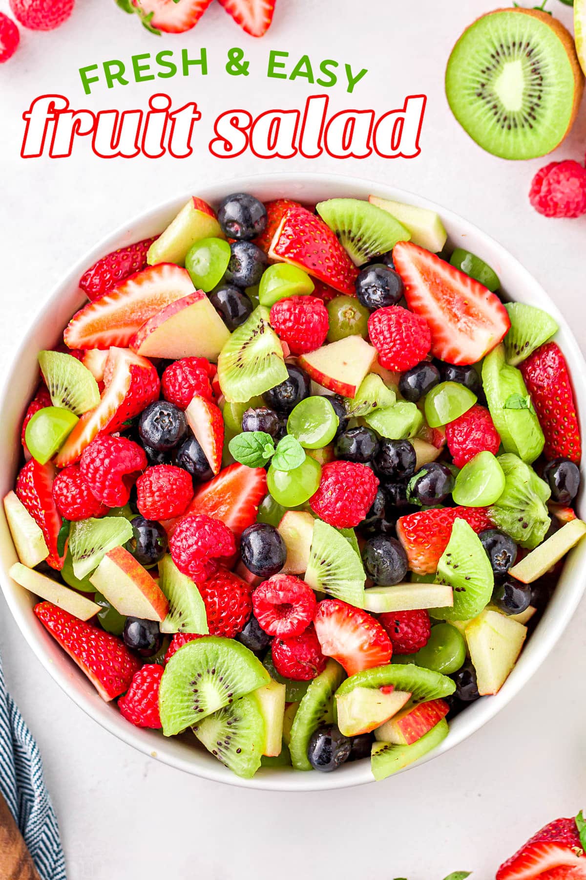 fruit salad in white bowl ready to serve with title overlay at top of image. fruit salad has kiwis, strawberries grapes and more.