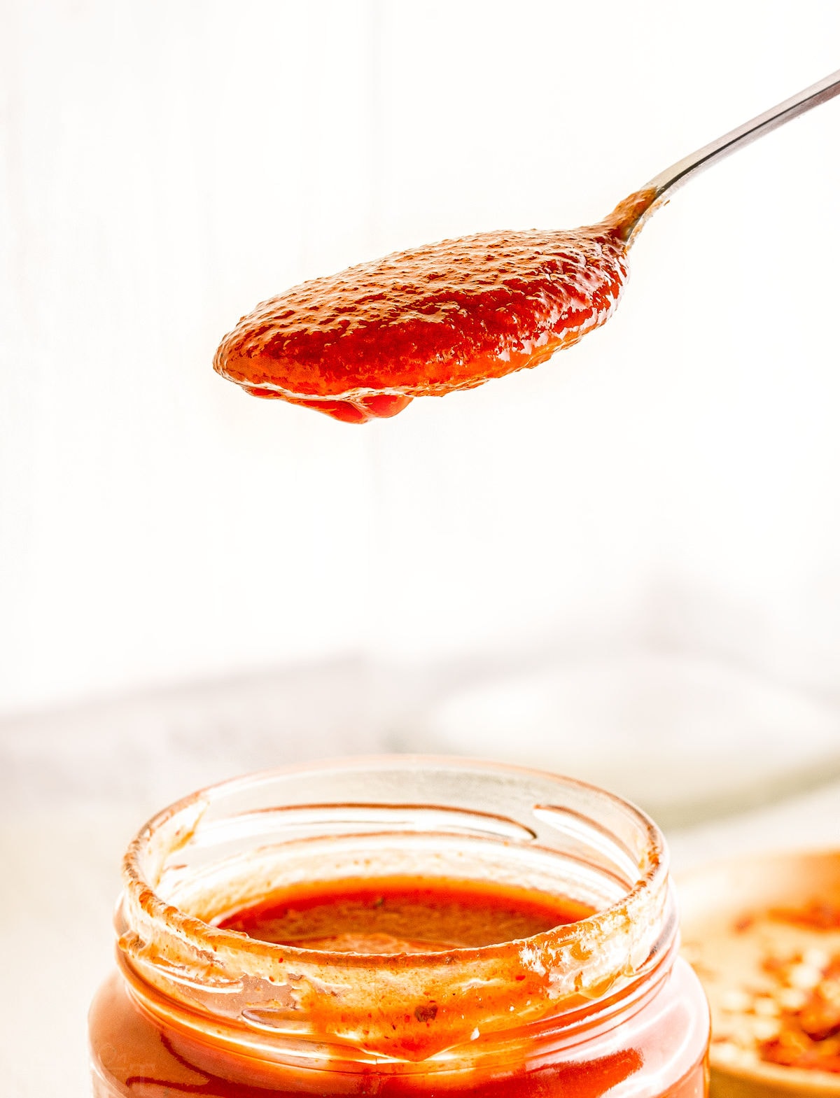 spoonful of homemade bbq sauce held above jar of bbq sauce.