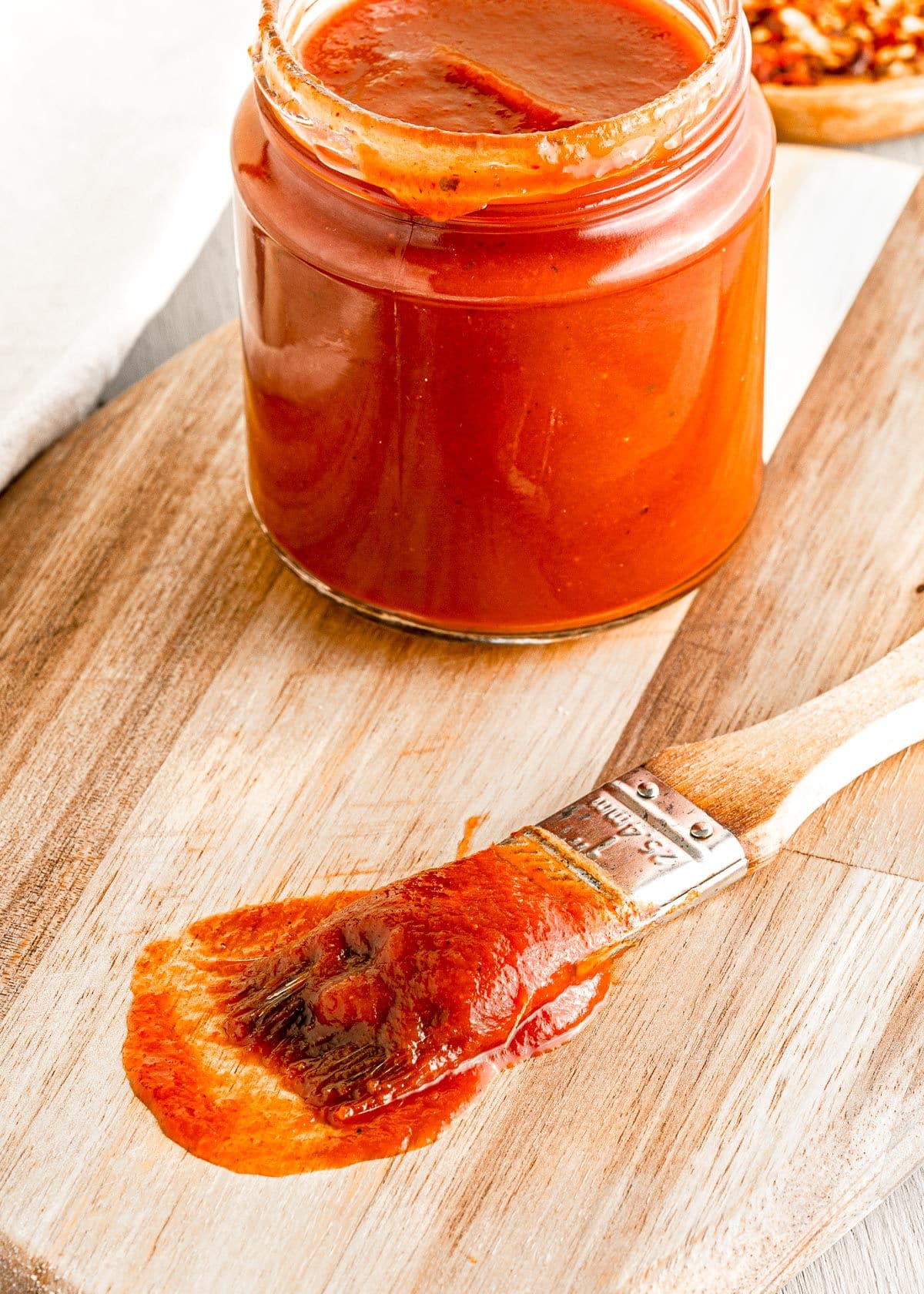 brush with bbq sauce on it sitting on cutting board next to a jar of bbq sauce.