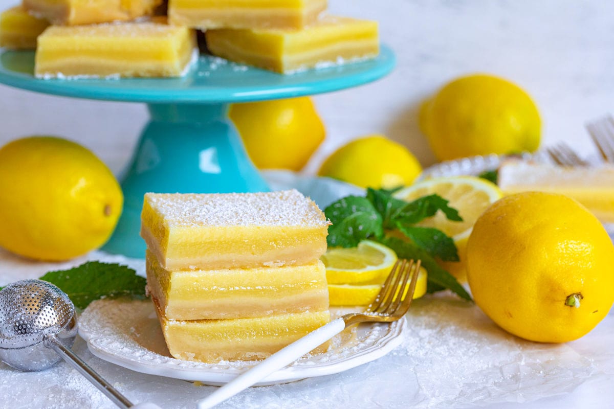lemon bars on plate and cake stand with fresh lemons and mint.
