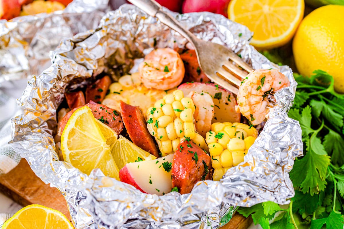 shrimp boil foil packs opened up and a shrimp on a fork ready to eat.