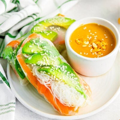 spring rolls on white plate with small bowl of peanut sauce to dip in on the side.