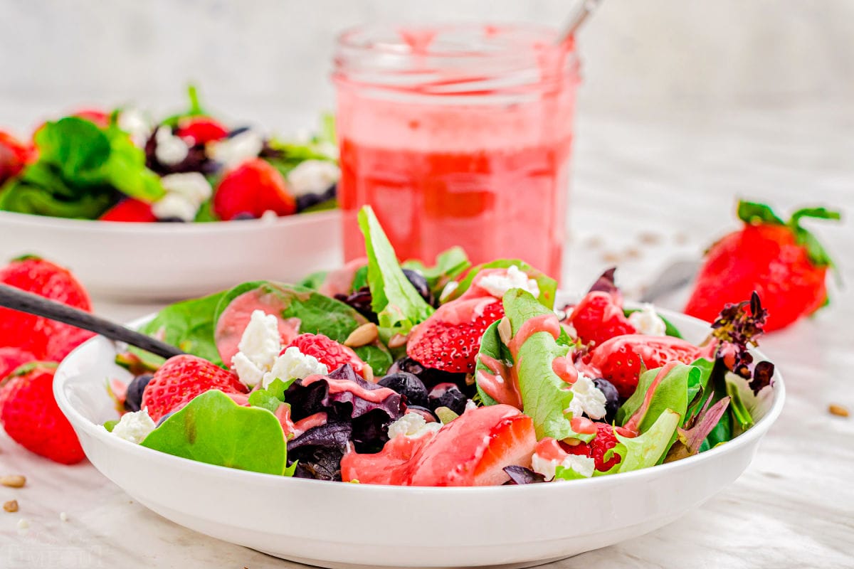 summer salad with berries and goat cheese on white plate.