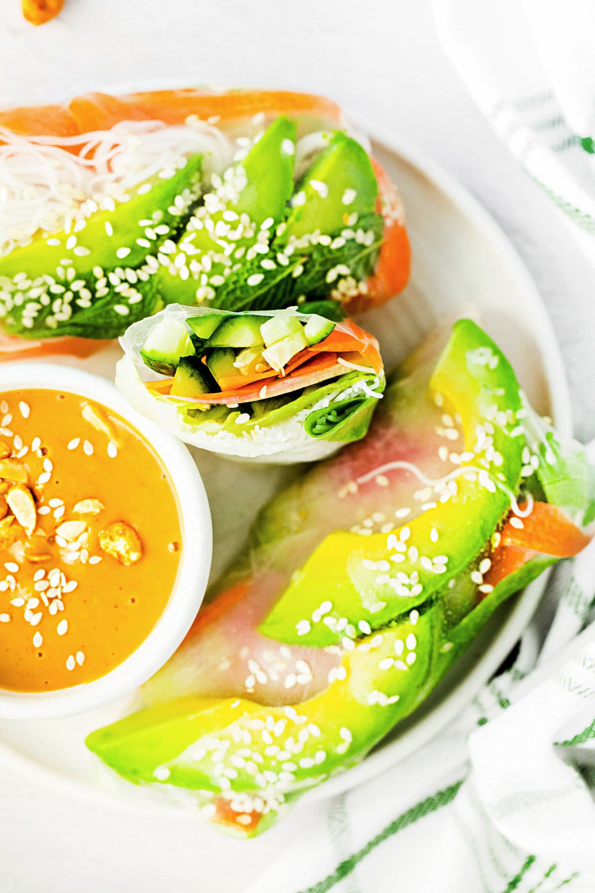 top down look at summer rolls on white plate with one cut in half. peanut dipping sauce in small bowl on the plate too.