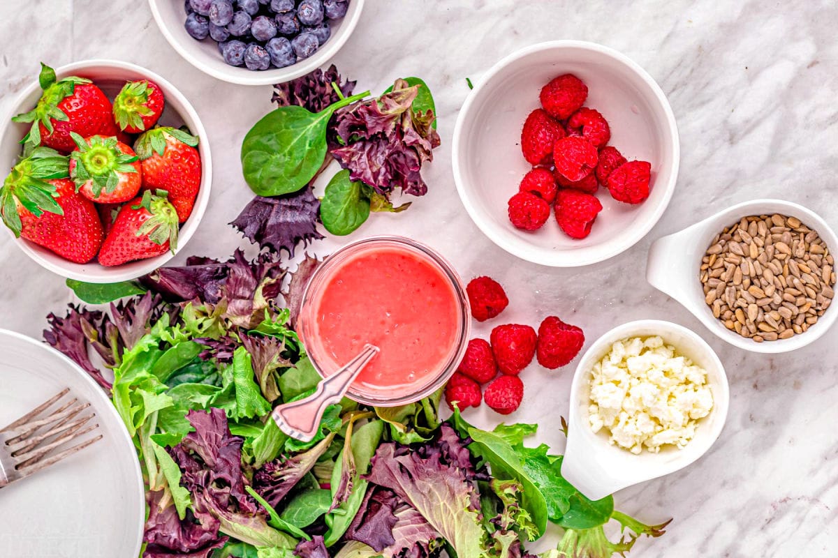 berry salad ingredients in various bowls sitting on marble surface.