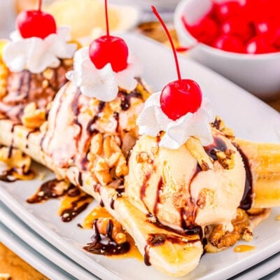 banana split on white plate topped with whipped cream and maraschino cherries.