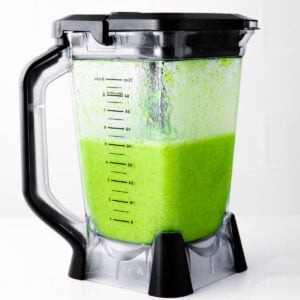green smoothie in blender with black detailing. the color is bright and vibrant and the smoothie is ready to be served.