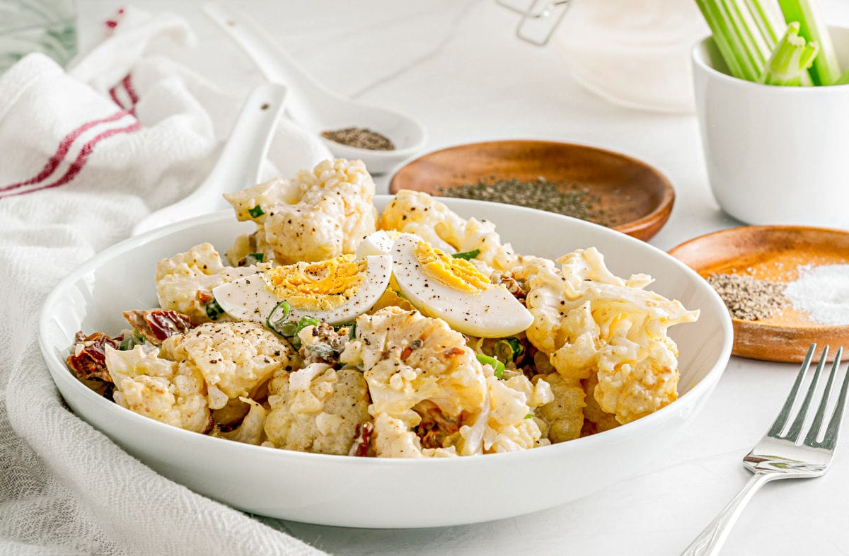 bowl of cauliflower potato salad topped with hard boiled egg quartered and sprinkled with pepper.