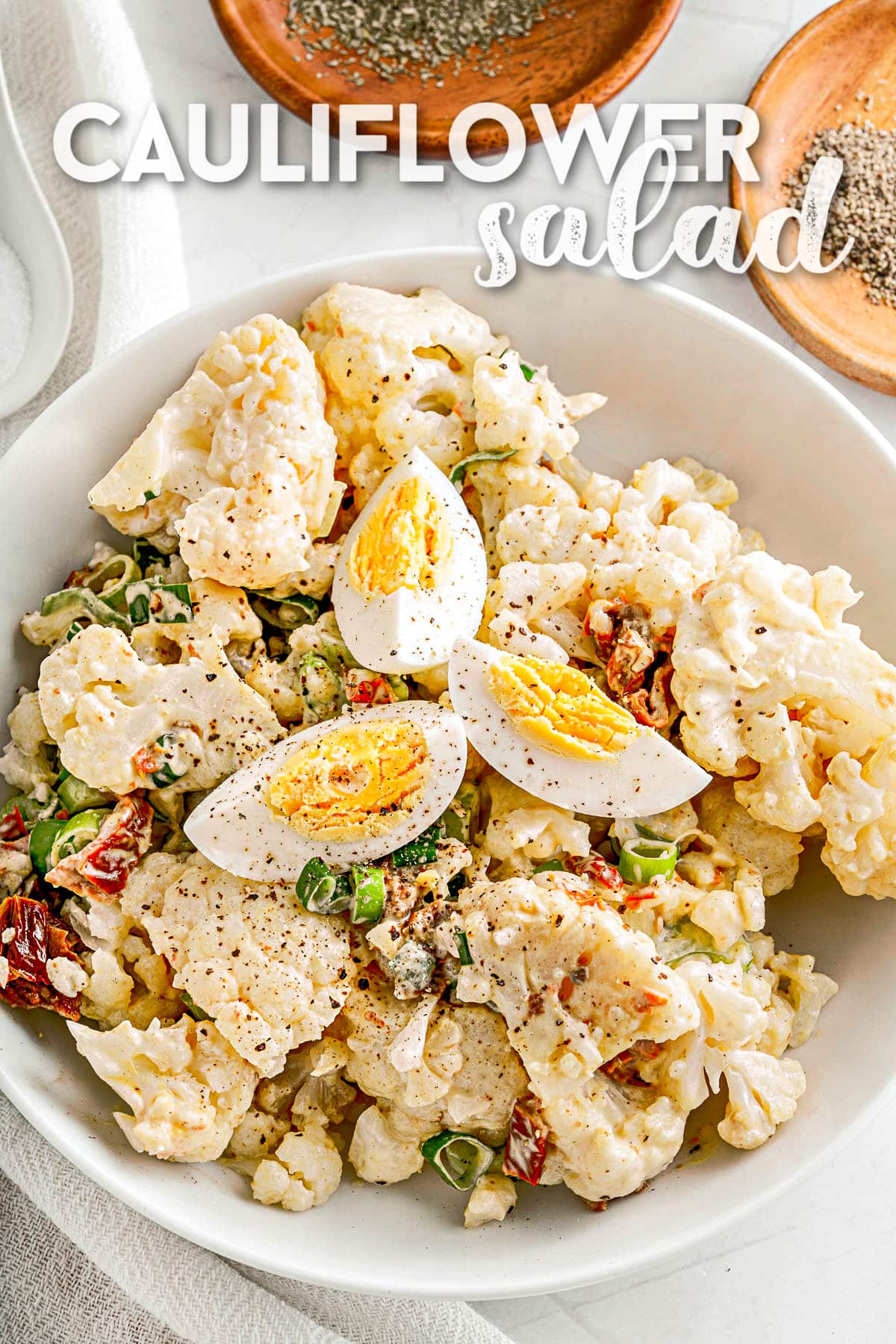 cauliflower salad made like a potato salad in white serving bowl and topped with slices of hard boiled egg. text overlay at top of image.