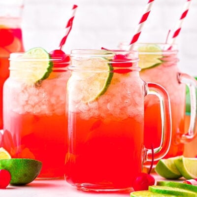 three mason jars filled with cherry limeade and garnished with lime slices and maraschino cherries.