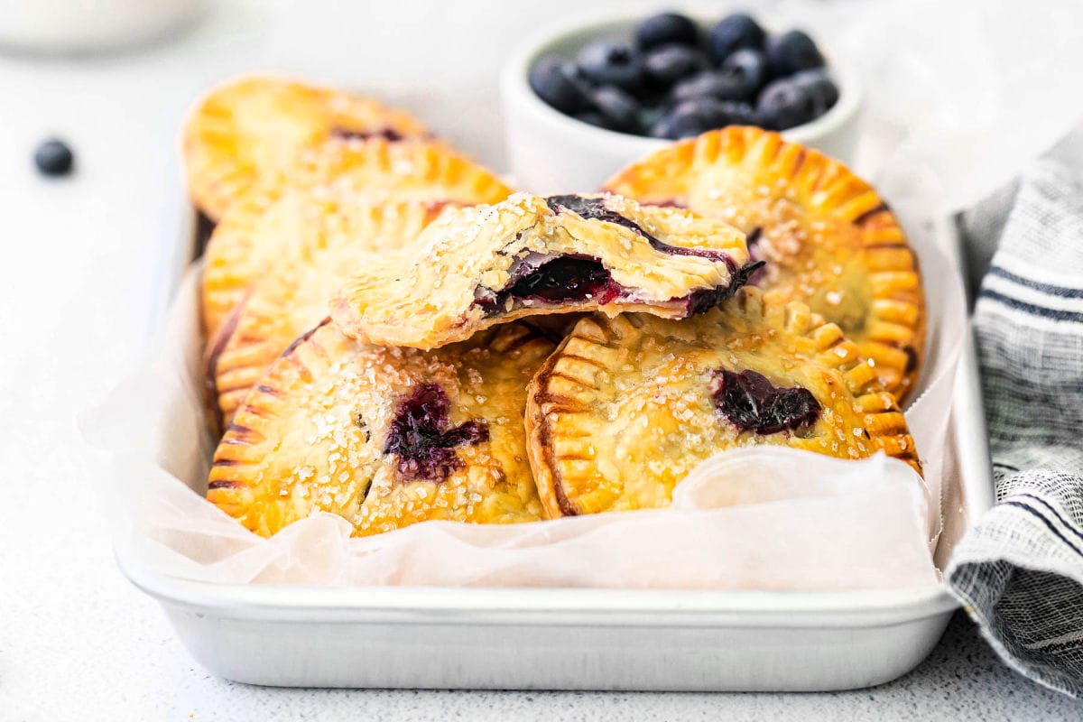 hand pie with blueberry filling broken in half so you can see the blueberry filling and sitting on more hand pies.