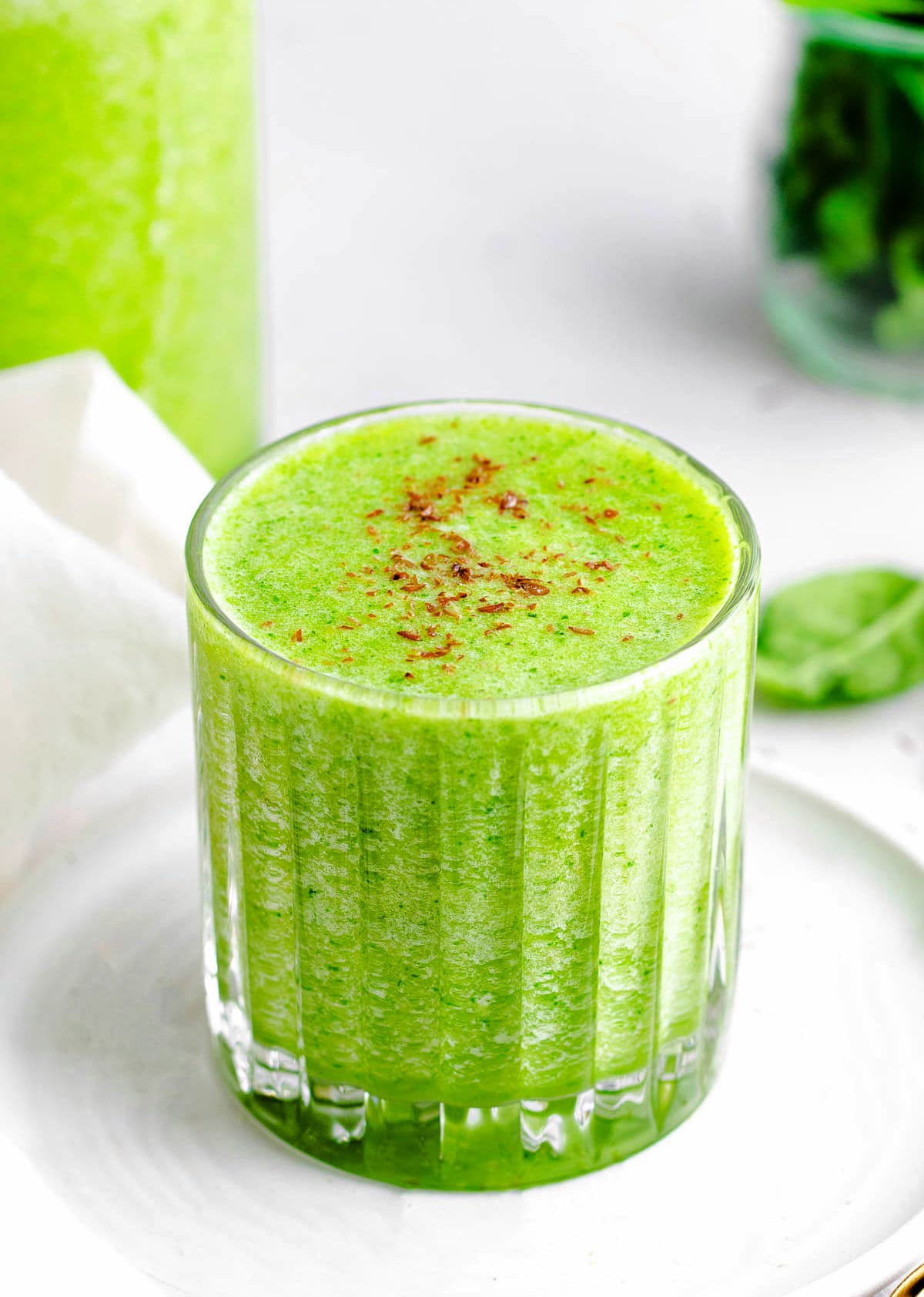 simple green smoothie recipe in glass sitting on small white plate in front of blender.