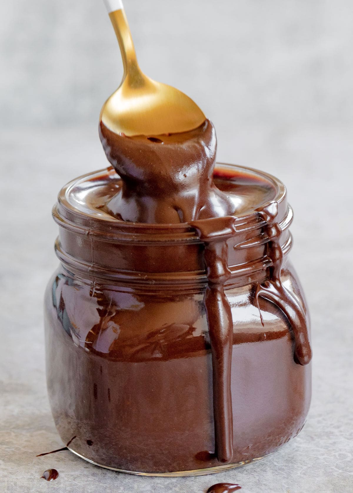 spoonful of hot fudge sauce held above glass jar.