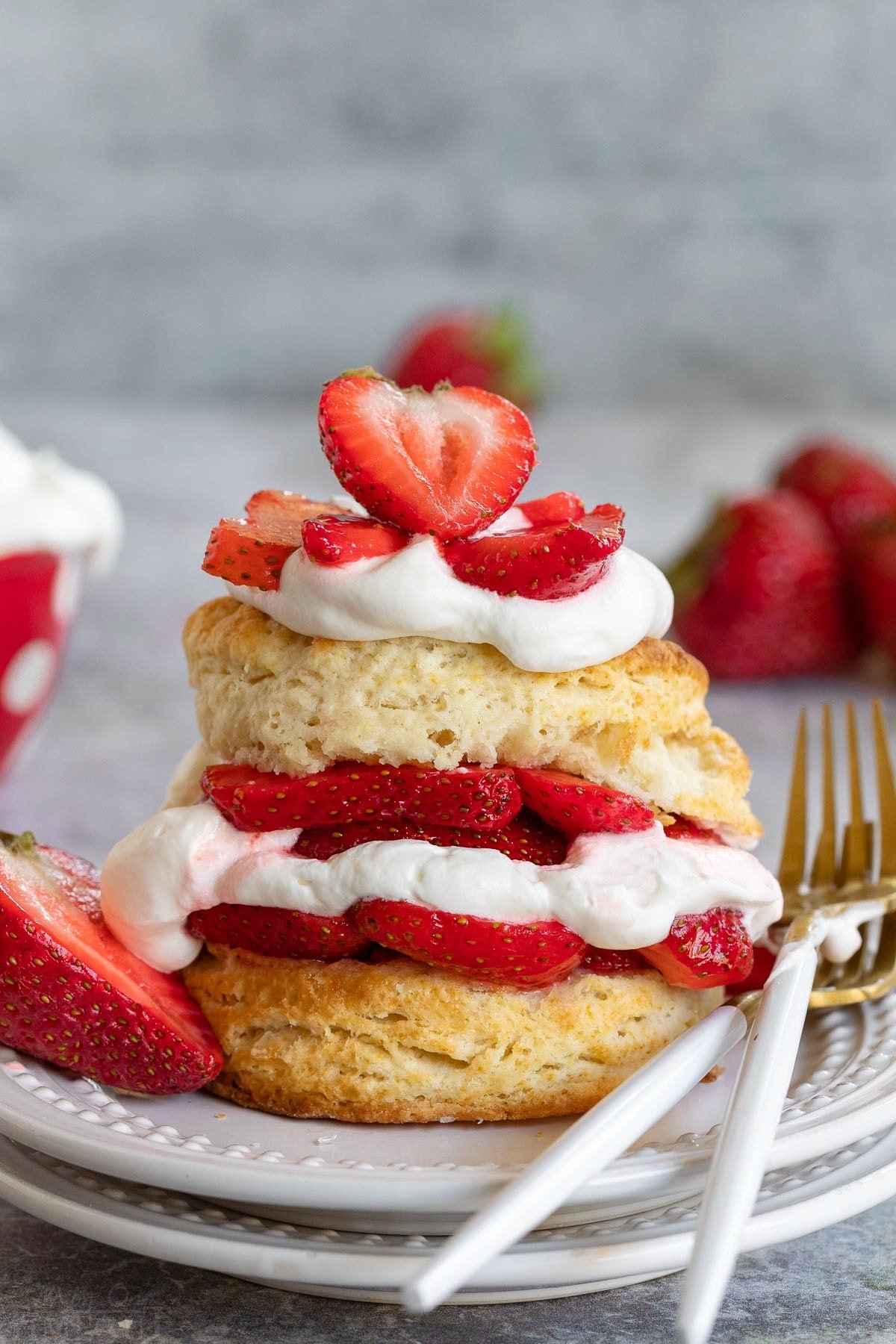 homemade strawberry shortcake on white plate with fresh macerated strawberries, whipped cream all layered on a split biscuit. 