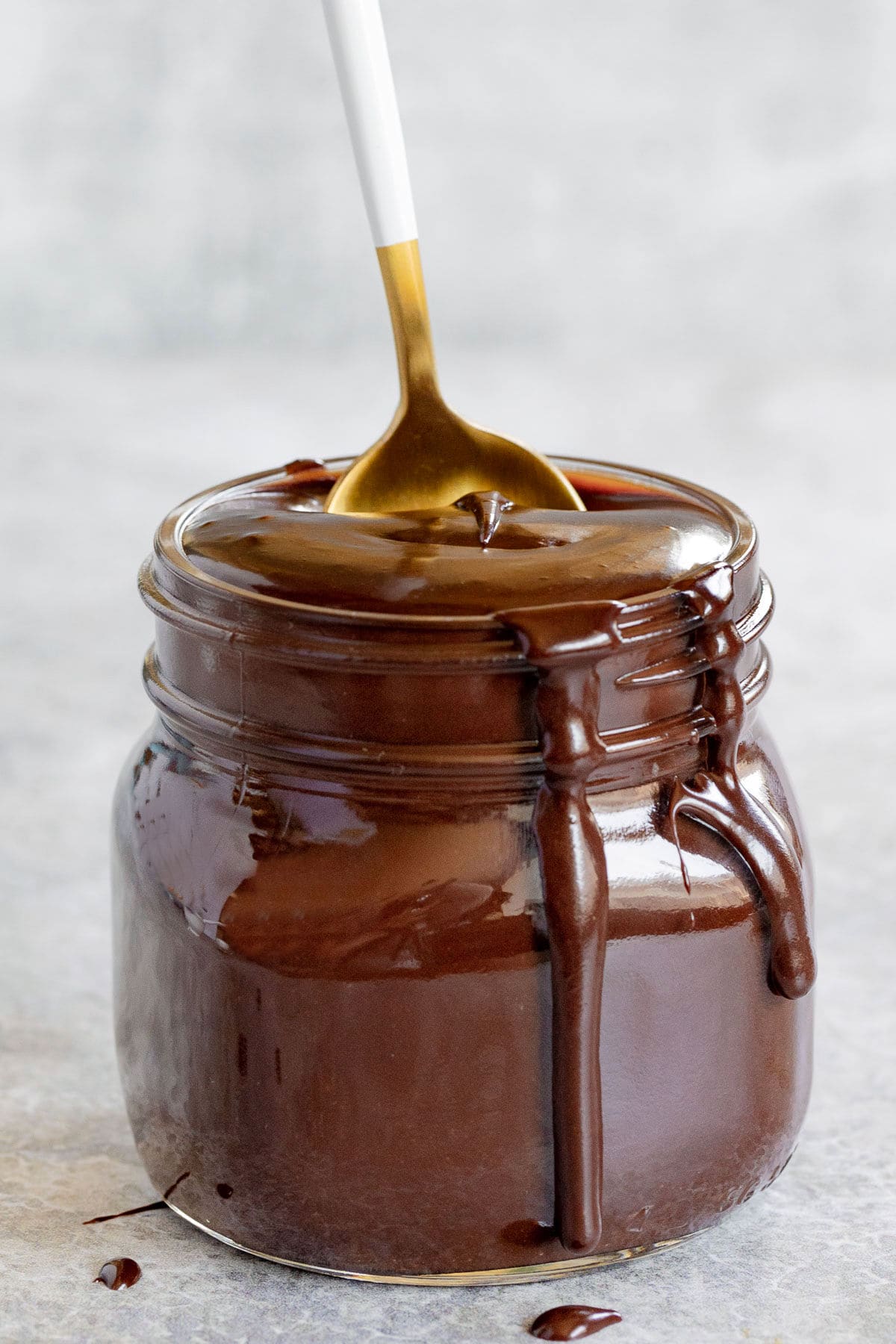 homemade hot fudge recipe in glass canning jar with gold and white spoon sticking out of it.