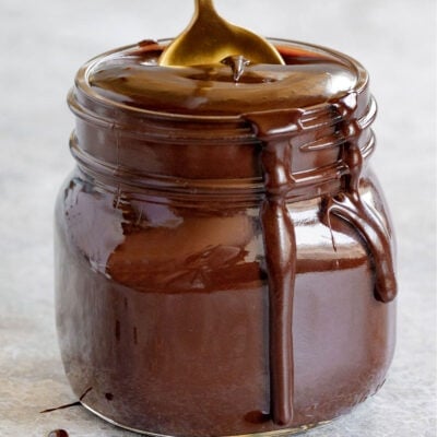 homemade hot fudge recipe in glass canning jar with gold and white spoon sticking out of it.