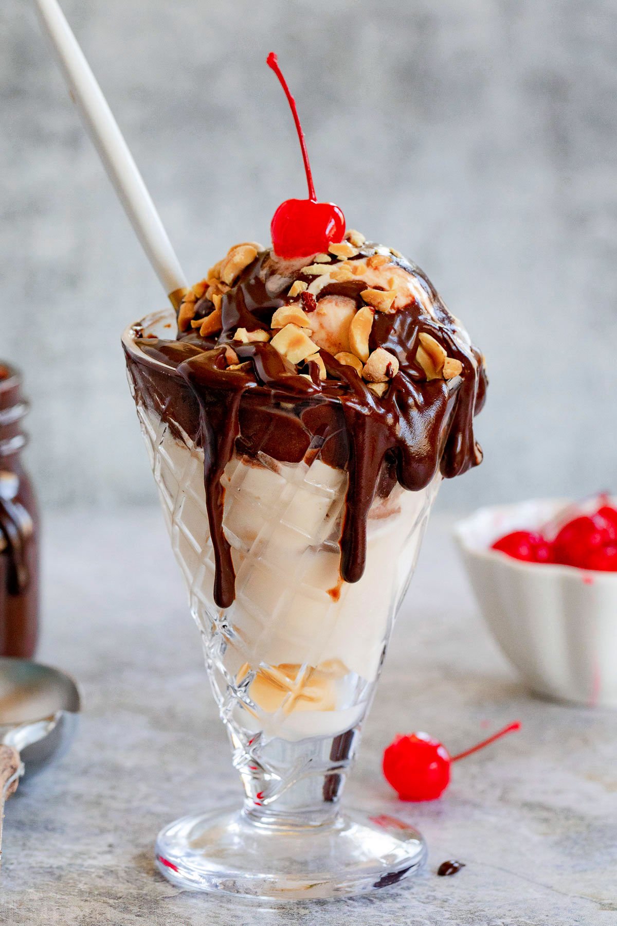 hot fudge sundae made with homemade hot fudge sauce, peanuts and a cherry on top. Served in glass cone with a white spoon.