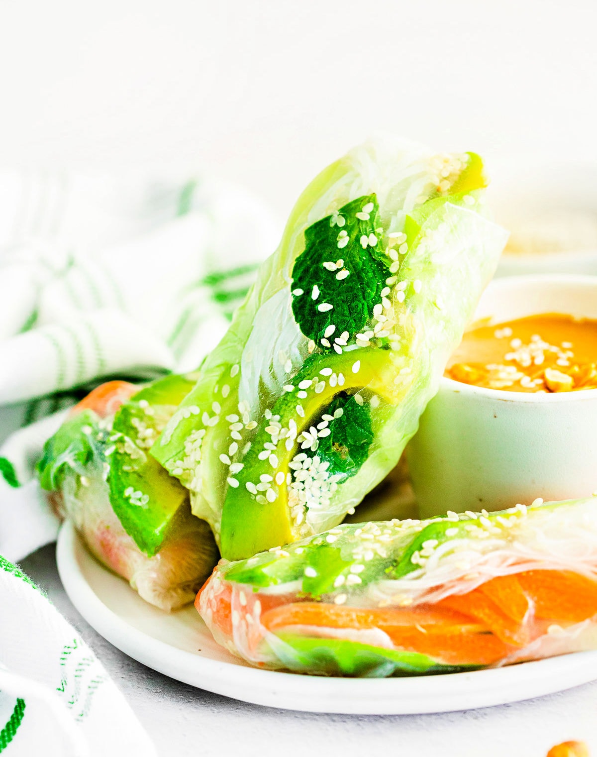 three summer rolls on white plate with peanut dipping sauce.