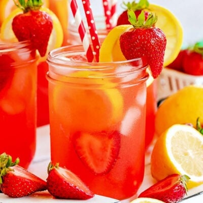 mason jars filled with strawberry lemonade and topped with lemon slices and fresh strawberries. Red and white paper straws in jars.