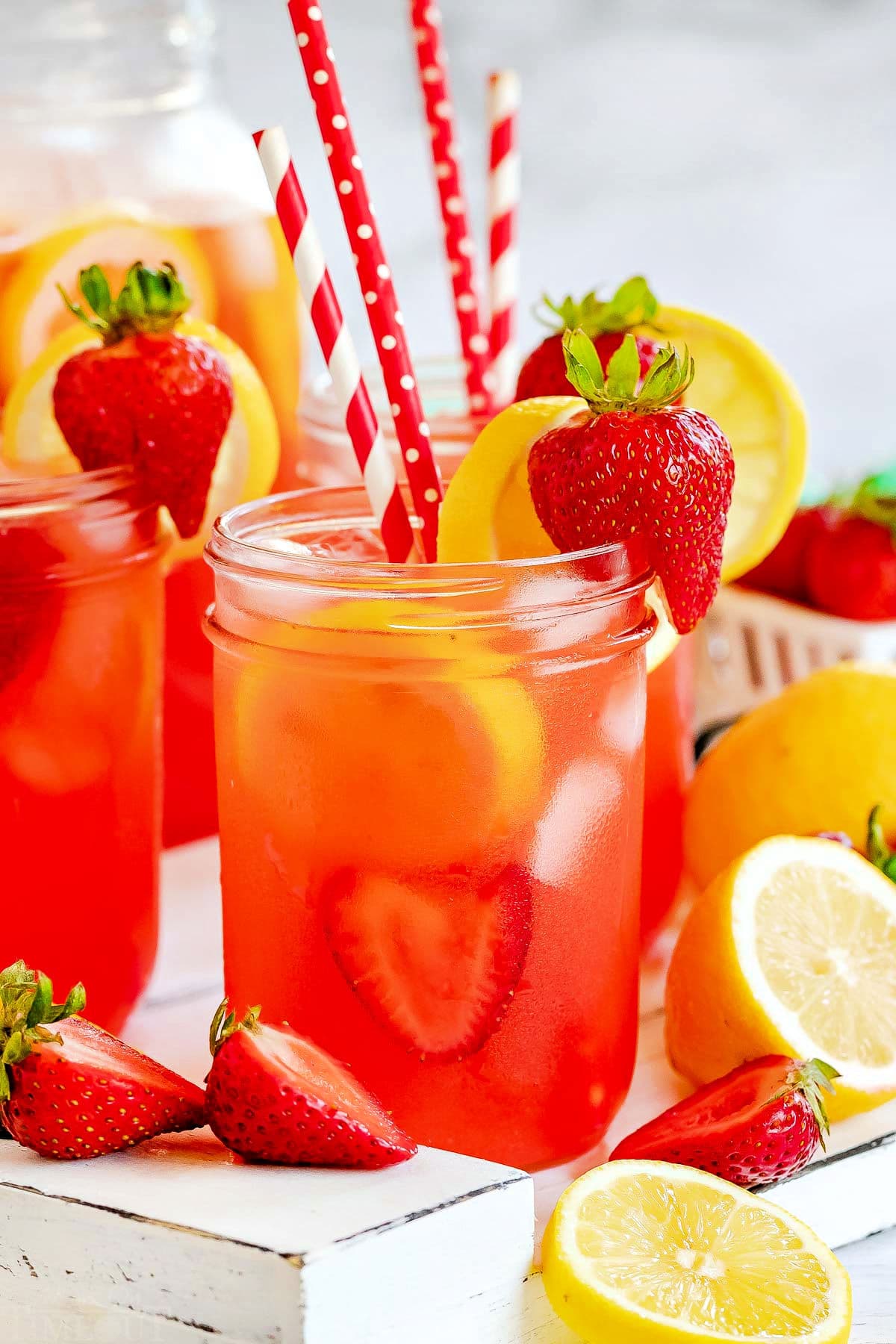 mason jars filled with strawberry lemonade and topped with lemon slices and fresh strawberries. Red and white paper straws in jars.