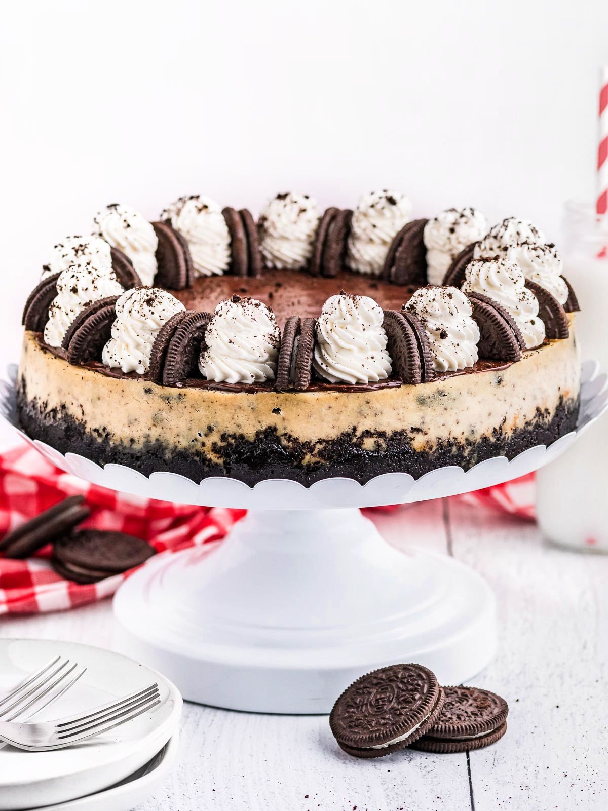 whole cheesecake made with oreos on a white metal cake stand and topped with whipped cream and oreo cookies.