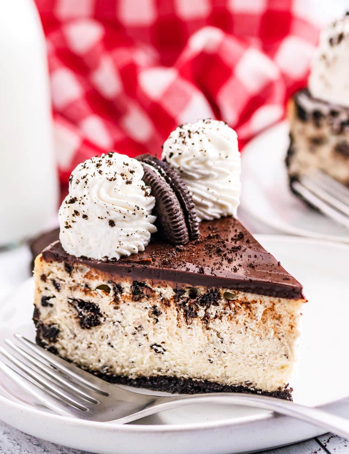 slice or oreo cheesecake sitting on white plate with red checkered napkin in background.