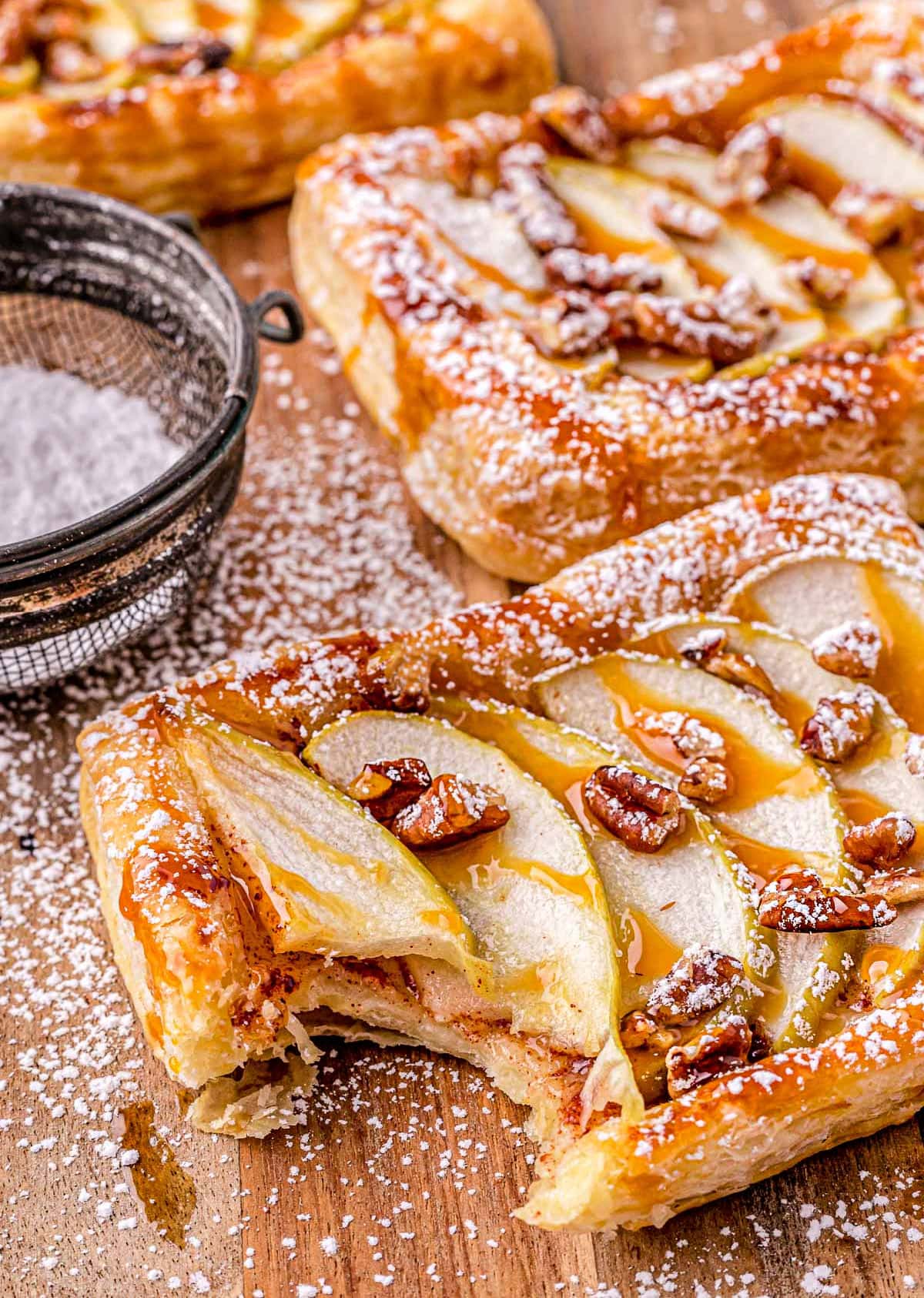 apple tart drizzled with caramel sauce and dusted with powdered sugar on a wood cutting board.