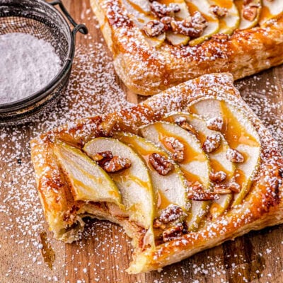 apple tart drizzled with caramel sauce and dusted with powdered sugar on a wood cutting board.