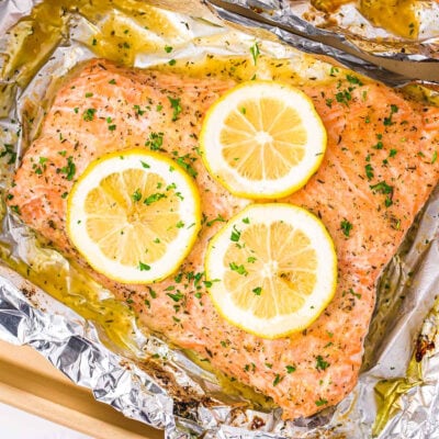 baked salmon in foil topped with lemon slices and fresh parsley.