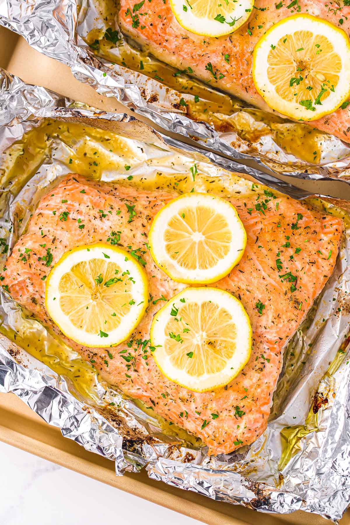 baked salmon in foil topped with lemon slices and fresh parsley. 