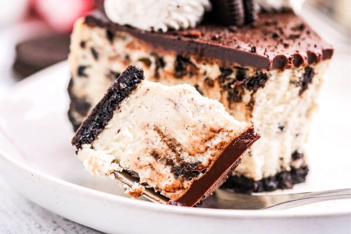 bite of oreo cheesecake sitting next to slice of cheesecake on a white plate.