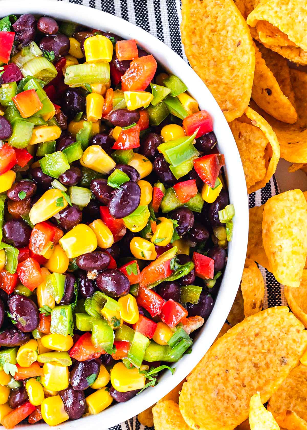 close up look at the vibrant colors of black bean and corn salsa in white bowl with corn chips around the bowl.