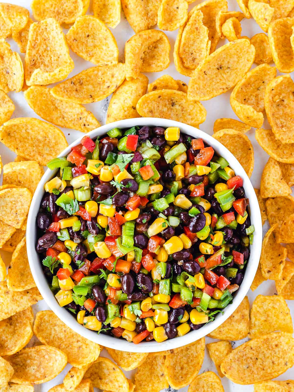 black bean corn salsa in small white serving bowl surround by large corn chips.