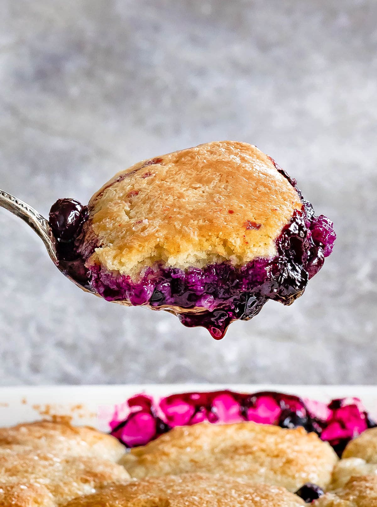 a scoop of blueberry cobbler held up over baking dish. 