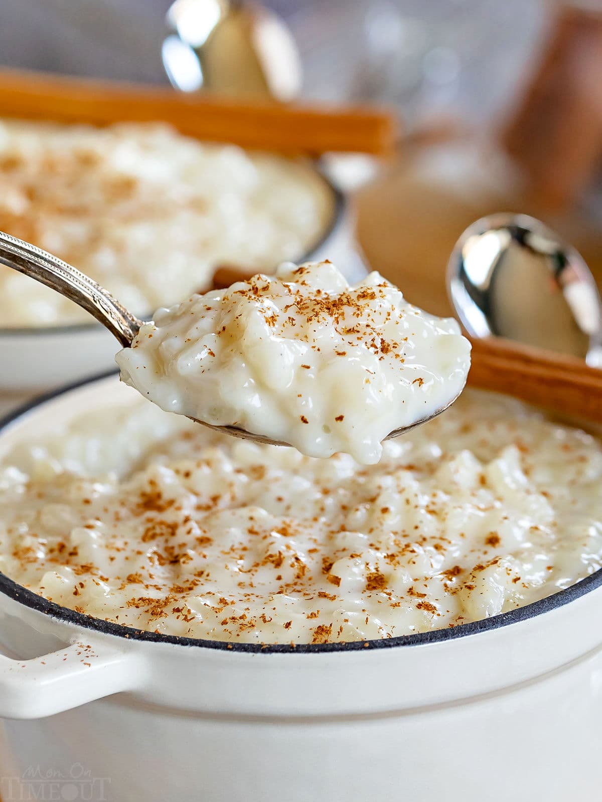 spoonful of rice pudding held up over the white pot it is being served from with freshly grated cinnamon stick on top.